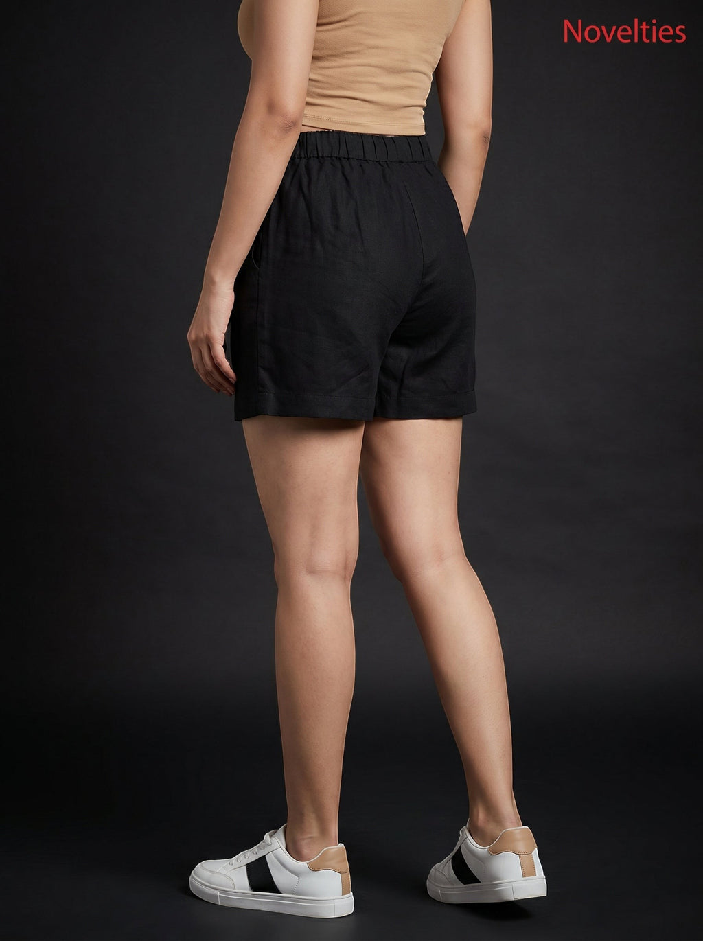 Model wearing black Novelties® pure cotton shorts with an elastic waistband, paired with a beige top and sneakers.