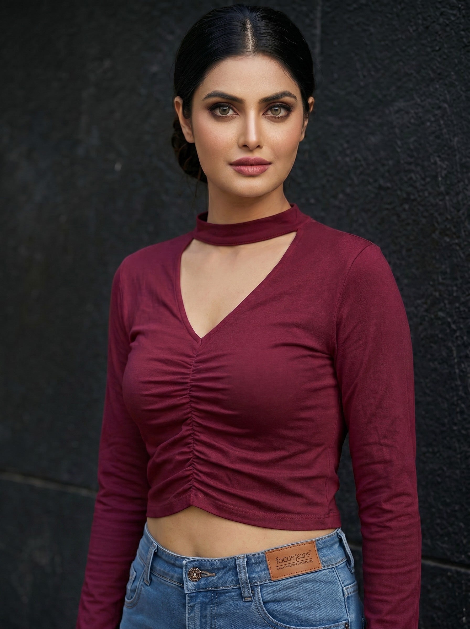 Model wearing a burgundy Novelties® long sleeve cropped top with a choker neck and ruched front V-cutout detail.