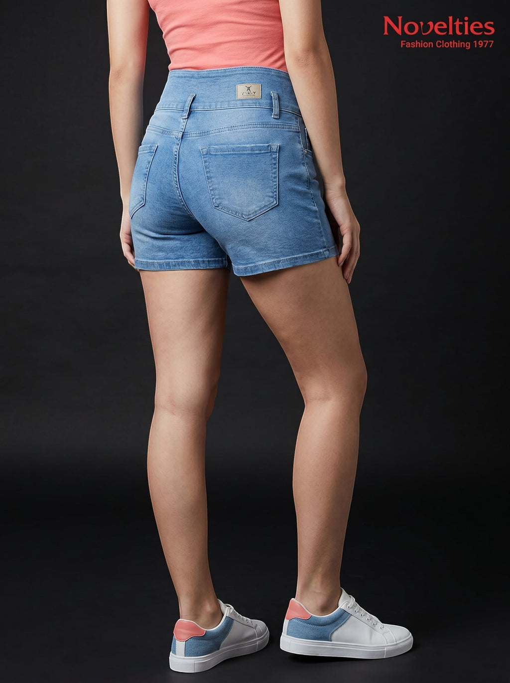 Model wearing Novelties® light blue high-waist denim hot shorts with back pockets against a black background.