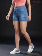 Model wearing Novelties® light blue high-waist denim hot shorts with triple-button closure and casual sneakers.