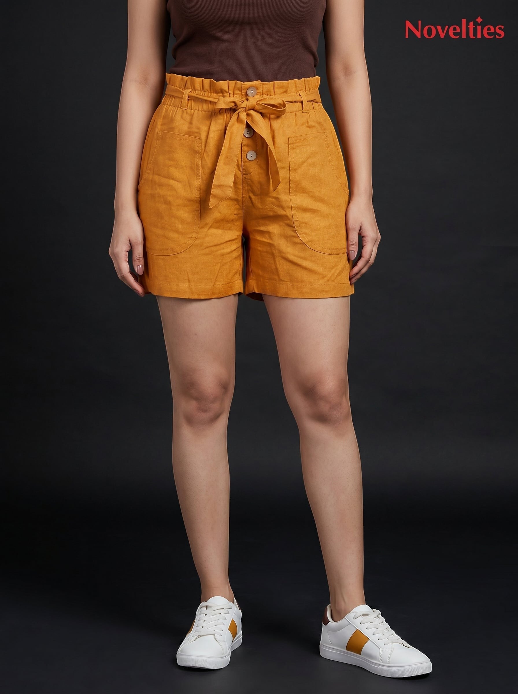 Model wearing Novelties® mustard pure cotton paperbag waist shorts with a self-tie belt and side pockets.
