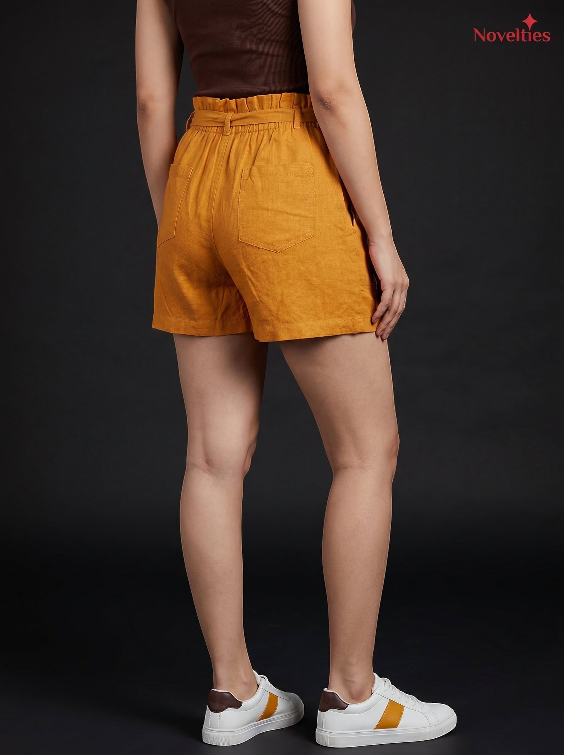 Model wearing Novelties® mustard pure cotton shorts with a paperbag waist and back patch pockets against black background