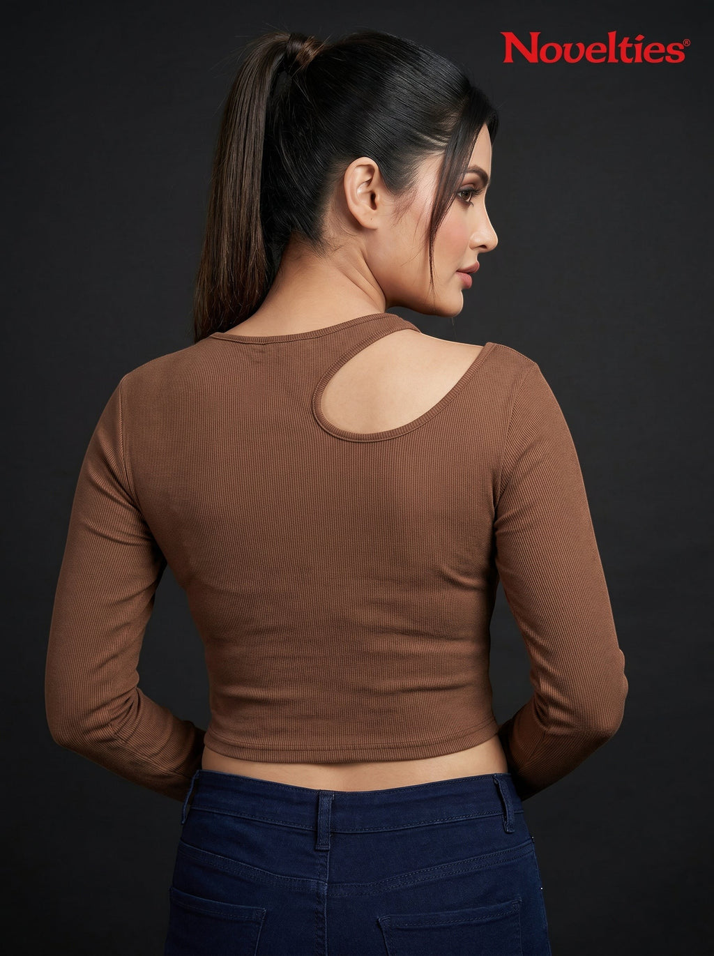 Model wearing a brown Novelties® ribbed long sleeve cropped top with an asymmetric shoulder cutout.