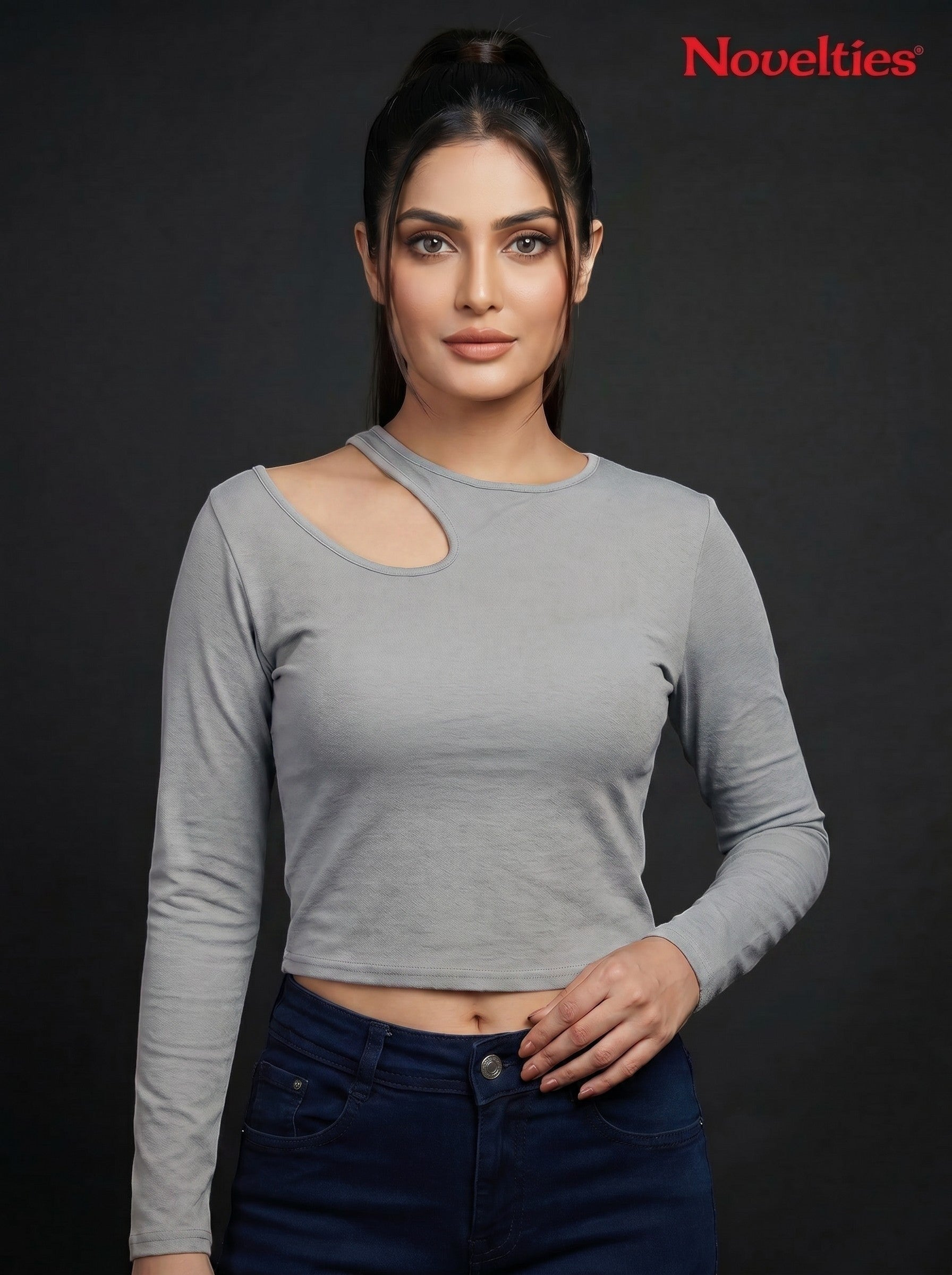 Model wearing a grey Novelties® ribbed long sleeve cropped top with an asymmetric shoulder cutout against black.