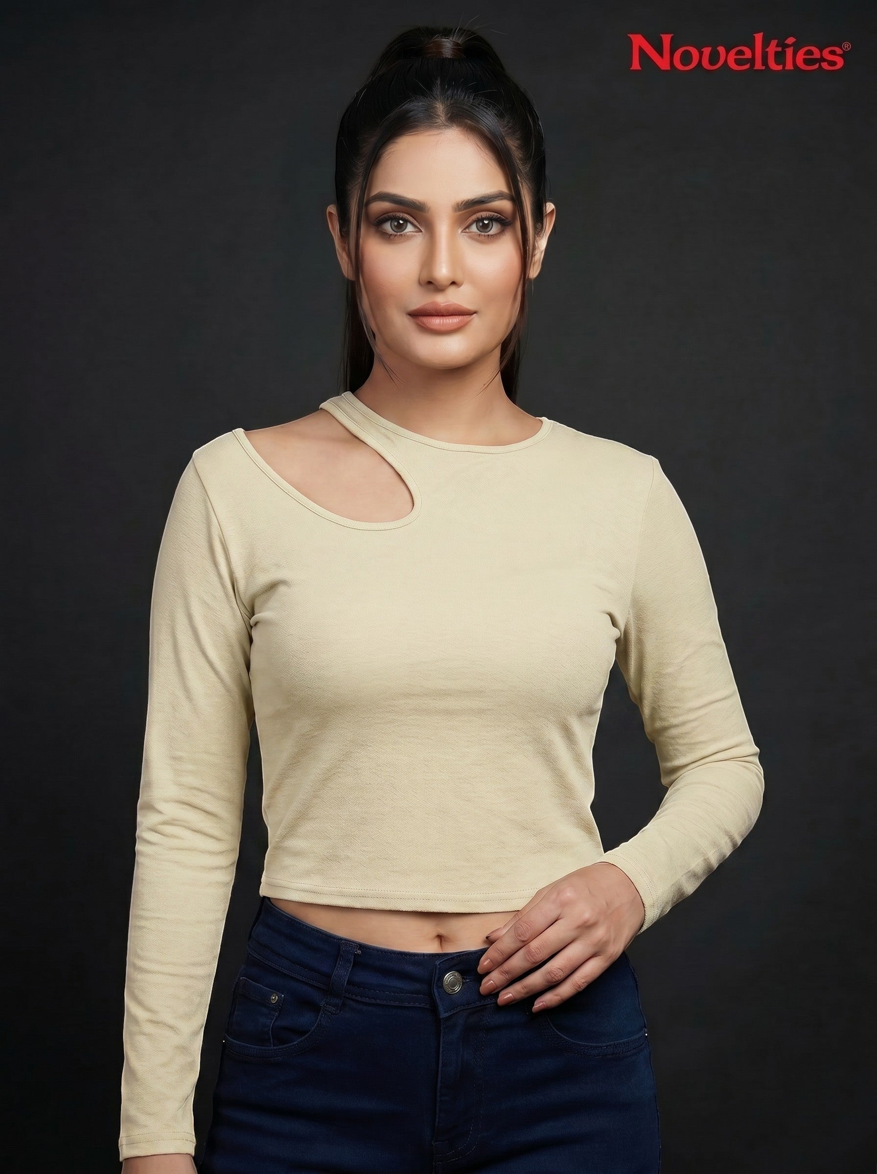 Model wearing a beige Novelties® ribbed long-sleeve cropped top with an asymmetric shoulder cutout and crew neck.