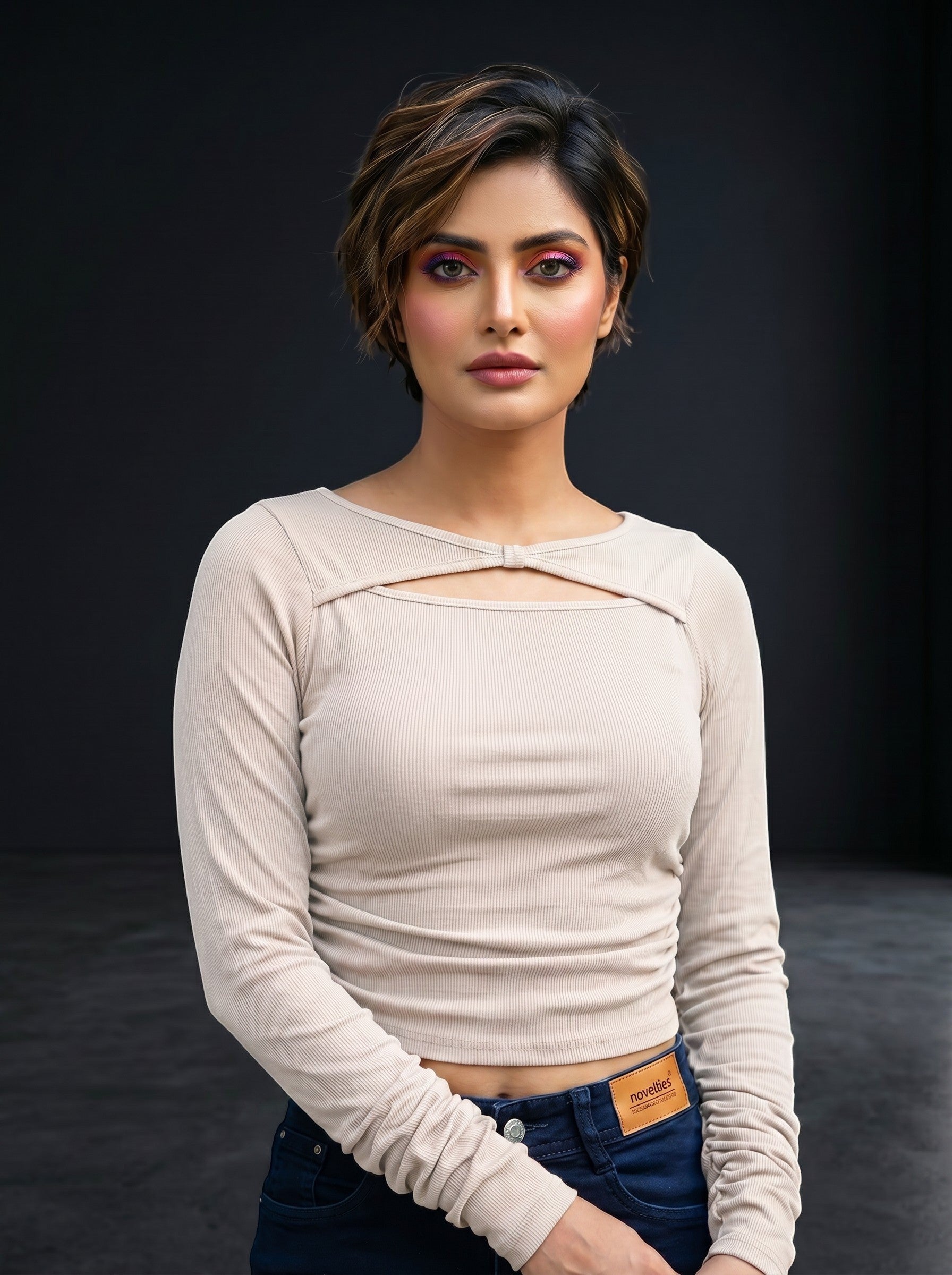 Model wearing a beige Novelties® ribbed long-sleeve crop top with a twist-front cutout and boat neckline.