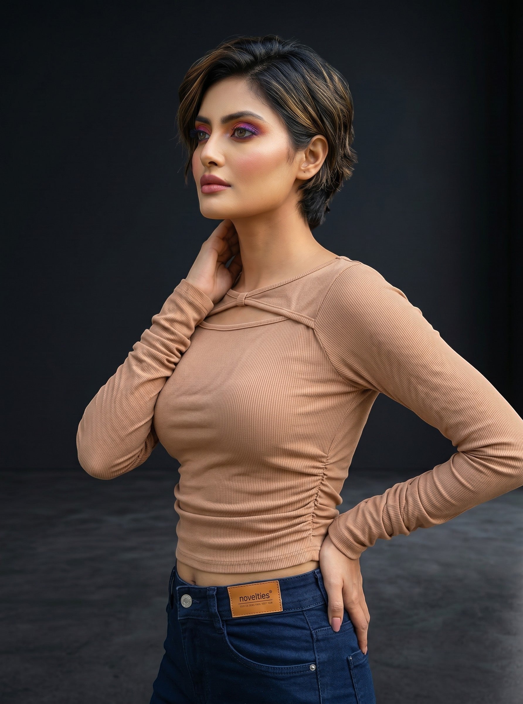 Model wearing a beige Novelties® ribbed long-sleeve crop top with a twist-front cutout and boat neckline.