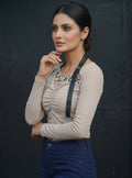Model wearing a beige Novelties® ruched long-sleeve crop top with a black graphic print and detachable strap detail.