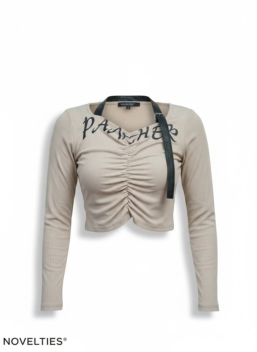Novelties® beige ribbed long-sleeve crop top with front ruching, black graphic script, and detachable strap detail.