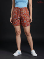 Model wearing Novelties® rust floral print shorts with an elastic drawstring waist against a black background.