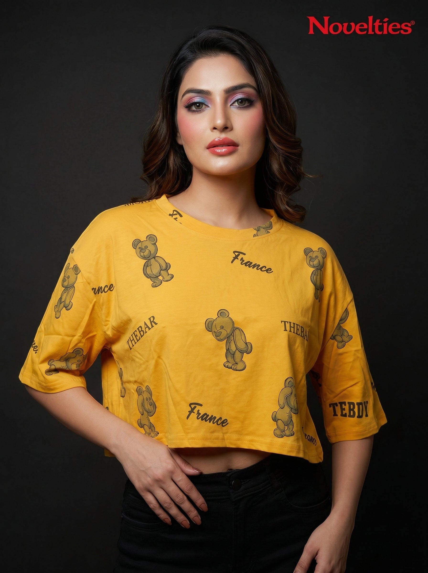 Model wearing a yellow Novelties® oversized crop tee with a playful teddy bear and slogan allover print.