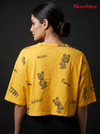 Model wearing a yellow Novelties® oversized crop tee with a playful teddy bear and slogan allover print.