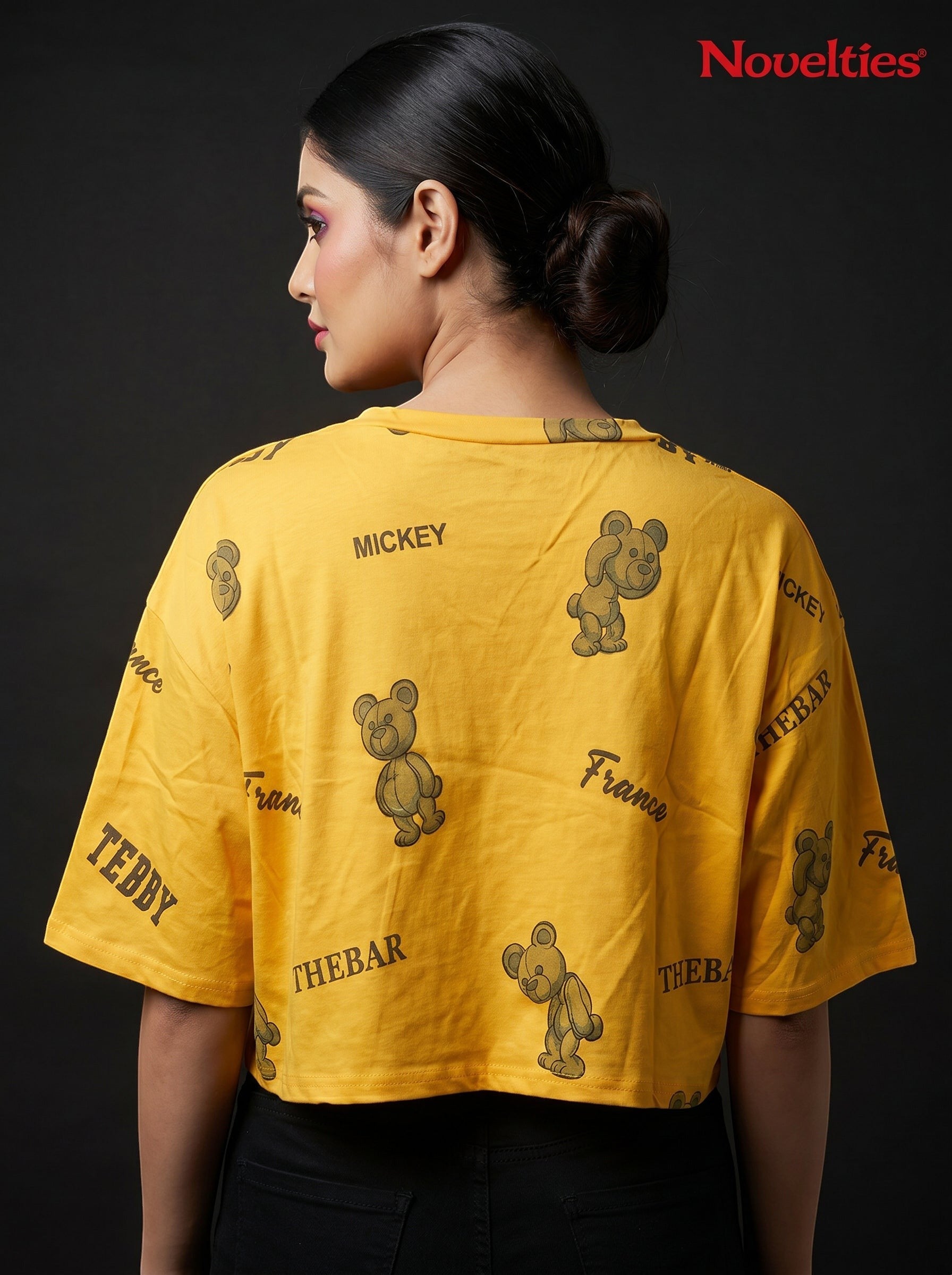 Model wearing a yellow Novelties® oversized crop tee with a playful teddy bear and slogan allover print.