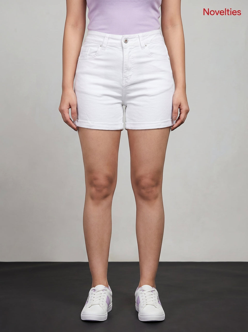 Model wearing Novelties® high-rise white denim shorts with a cuffed hem, paired with a lavender top and white sneakers.