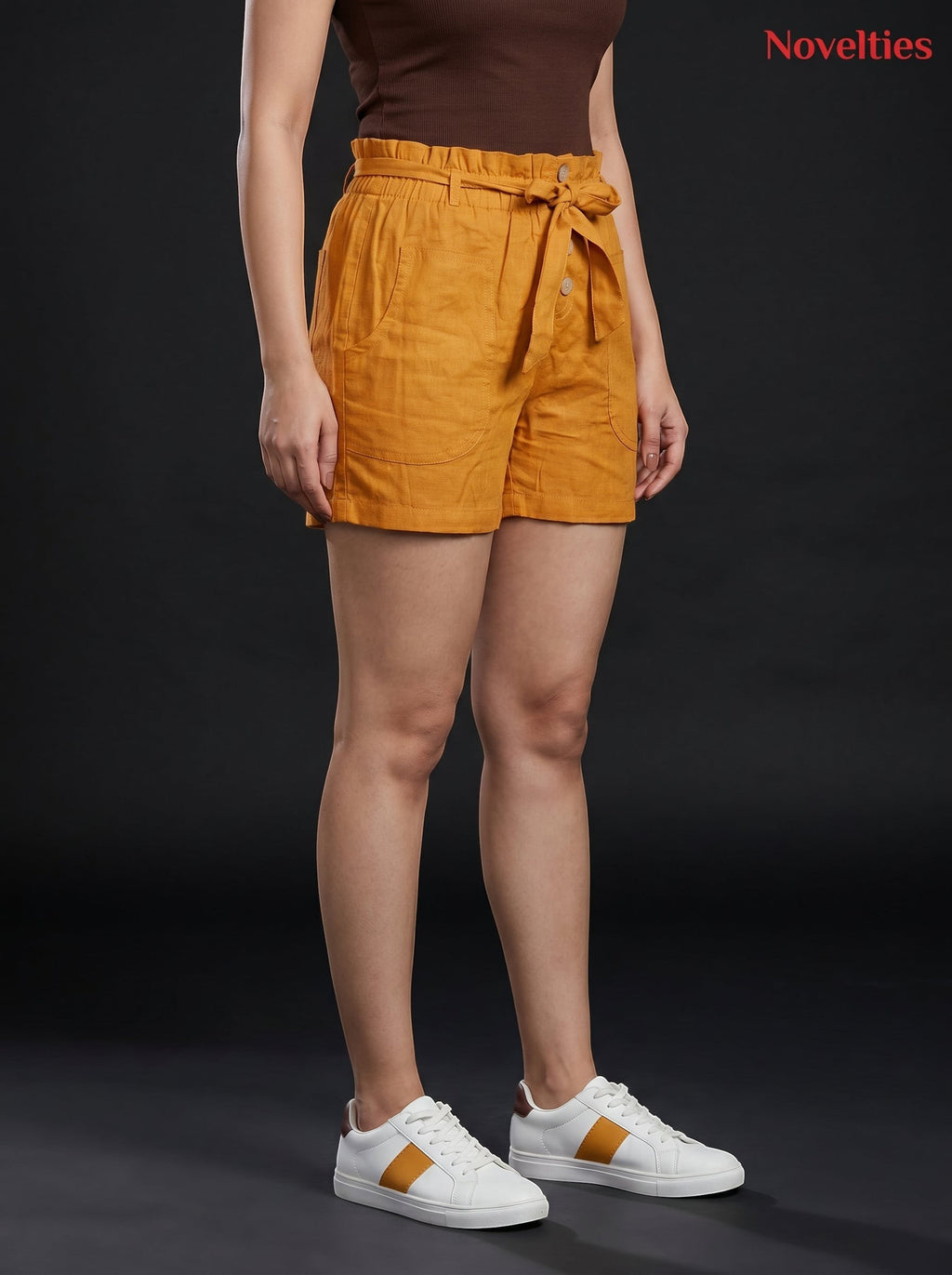 Model wearing Novelties® mustard pure cotton shorts with a paperbag waist, tie belt, and side pockets.