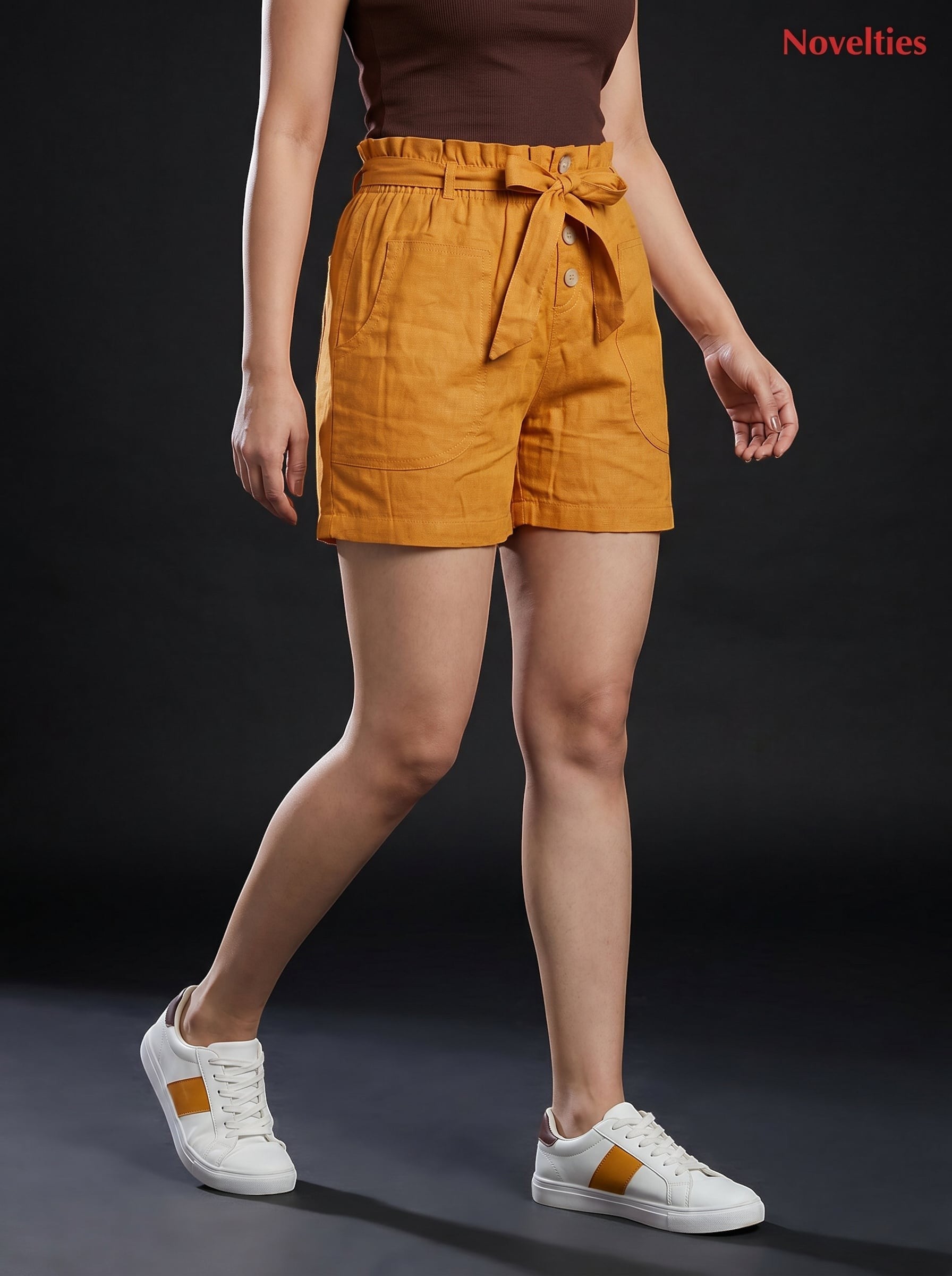 Model wearing Novelties® mustard pure cotton shorts with a paperbag waist, tie belt, and side pockets.